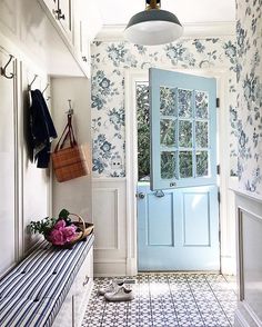 a blue front door in a white and blue tiled entryway with floral wallpaper