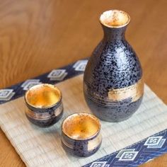 three cups and a vase sitting on a place mat with a blue napkin around it