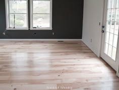 an empty room with hard wood floors and two windows in the corner that are painted gray