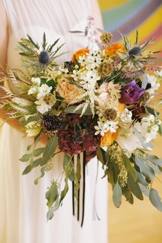 a woman holding a bouquet of flowers and greenery in front of a colorful background