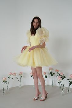 Introducing the Britney Dress in a delightful light yellow: a stunning creation crafted from delicate bubble organza. This lightweight dress features an elegant silhouette with a voluminous floating skirt that moves gracefully with every step. The charming puff sleeves add a whimsical touch, making it perfect for any special occasion. The Britney Dress is enclosed with delicate bow ties down the back, adding a romantic and feminine detail that completes the look. In light yellow, this dress exud Summer Cream Organza Dress, Cream Organza Dress For Summer, Organza Puff Sleeve Wedding Dress, Yellow Organza Wedding Dress, Spring Party Puff Sleeve Dress With Voluminous Skirt, Feminine Yellow Evening Dress, Spring Cream Organza Dresses, Cream Puff Sleeve Party Dress, Cream Puff Sleeve Dress For Party