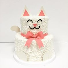 a white cake with a cat on top and pink ribbon around the edge, sitting on a plate