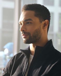 a close up of a person wearing a jacket and looking off into the distance with buildings in the background