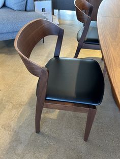 a wooden chair with black leather upholstered seat and back rests on the carpeted floor