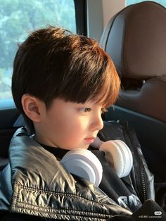 a young boy sitting in the back seat of a car with headphones around his neck