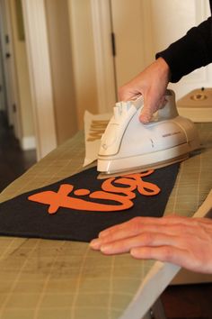 a person ironing an orange and black t - shirt on top of a table