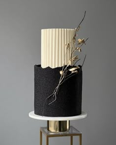 a black and white cake with gold decoration on a small stand against a gray wall