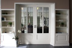 an empty room with white bookcases and glass front doors that lead into the dining area