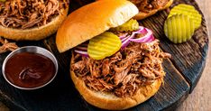 two pulled pork sandwiches with pickles and ketchup on a wooden platter