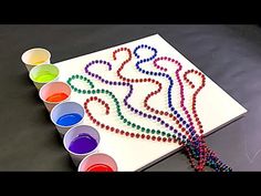 a table topped with lots of paint next to cups filled with colored water and beads