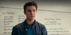 a young man standing in front of a whiteboard with writing on the wall behind him