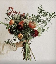 a person holding a bouquet of flowers in their hand with greenery on the side