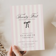 a person holding up a pink and white striped wedding card with a bow on it