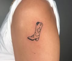 a woman's arm with a small tattoo of a cowboy boot on the left shoulder