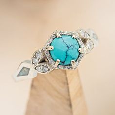 a turquoise stone surrounded by diamonds sits on a wooden stand