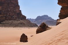 two large rocks sitting in the middle of a sandy area with mountains in the background