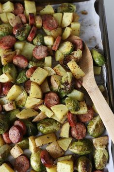 a pan filled with potatoes, brussels sprouts and sausage next to a wooden spoon