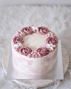 a white cake with pink frosting and flowers on top is sitting on a plate