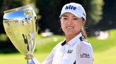 a woman is holding up a trophy in front of her face on the golf course