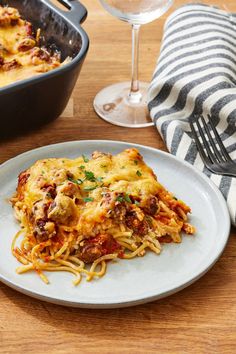 a white plate topped with lasagna next to a glass of wine and a dish