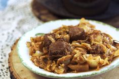 a white plate topped with meat and noodles on top of a wooden table next to a pot