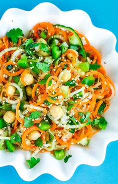 a salad with carrots, green beans and sesame seeds in a white bowl on a blue surface