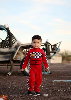 a young boy in a red and black suit standing next to an airplane on the ground