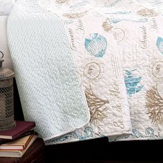 a bed with a white and blue quilt on top of it next to a lamp