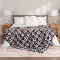 a bed covered in a plaid blanket with pillows and two lamps on either side of it