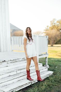 a woman wearing red cowboy boots standing in front of a white porch with steps and grass