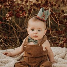 a baby is sitting on a blanket wearing a bow tie and a brown overalls