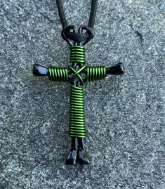 a cross made out of green and black wires on top of a gray surface with a black leather cord