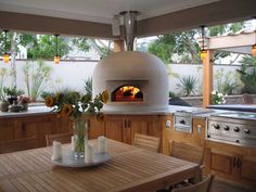 an outdoor kitchen with a wood burning oven and sunflowers in the vase on the table