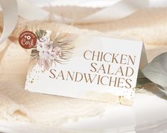 there is a sign that says chicken salad sandwiches next to a flower on a plate