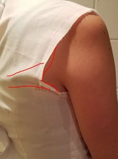 the back of a woman's white shirt with red stitching on her left shoulder