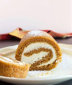 a piece of cake on a plate with powdered sugar next to it and a roll in the middle