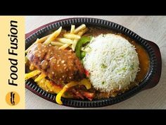 a black plate topped with rice and meat covered in gravy next to fries