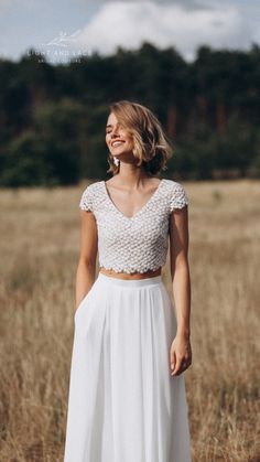 a woman standing in a field wearing a white skirt and crop top with short sleeves