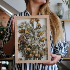 a woman holding up a frame with flowers in it