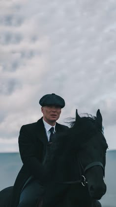 a man in a suit riding on the back of a black horse next to water