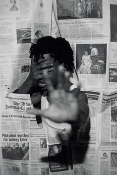 a black and white photo of a woman covering her face with her hands while standing in front of newspapers