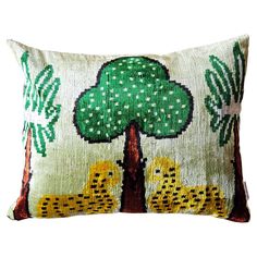 a green and yellow pillow with two cheetah on the front, sitting under a tree