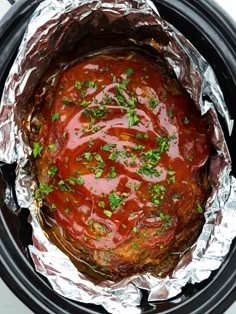 an open crock pot filled with meat covered in sauce and garnished with parsley