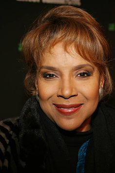 a close up of a person wearing a black coat and smiling at the camera with her hair pulled back