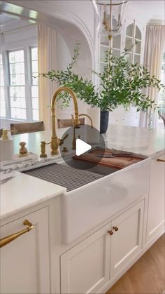 a kitchen with white cabinets and gold faucets on the counter top, along with a potted plant