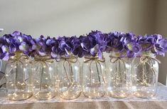 purple flowers are in glass jars with string lights