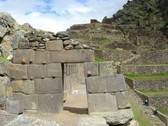 the entrance to an ancient building with stone walls and steps leading up to it, surrounded by large rocks