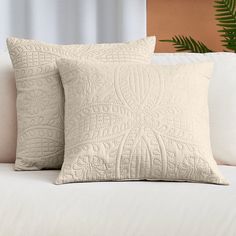 two pillows on a white couch next to a potted plant