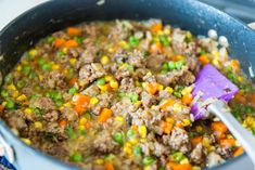 a pot filled with meat and vegetables on top of a stove next to a purple spatula