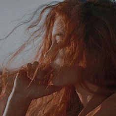 a woman with long red hair blowing her hair in the wind and looking off into the distance